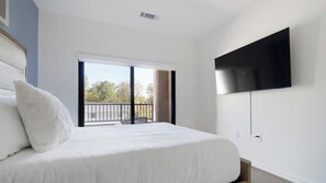A bedroom with a large bed, a flat-screen TV mounted on the wall, and a sliding glass door leading to an outdoor balcony.