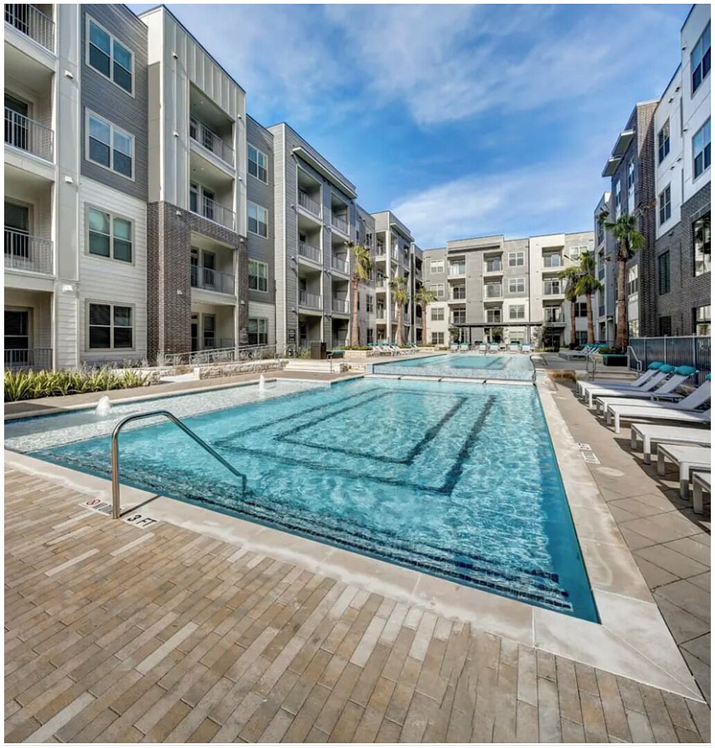 A modern apartment building with a central swimming pool, multiple balconies, and a brick pathway.