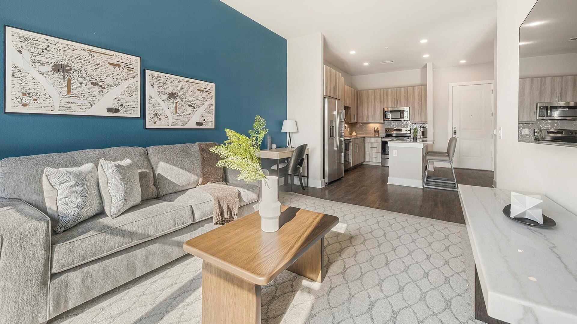 A modern living room with a grey sofa, a wooden coffee table, and a blue accent wall.
