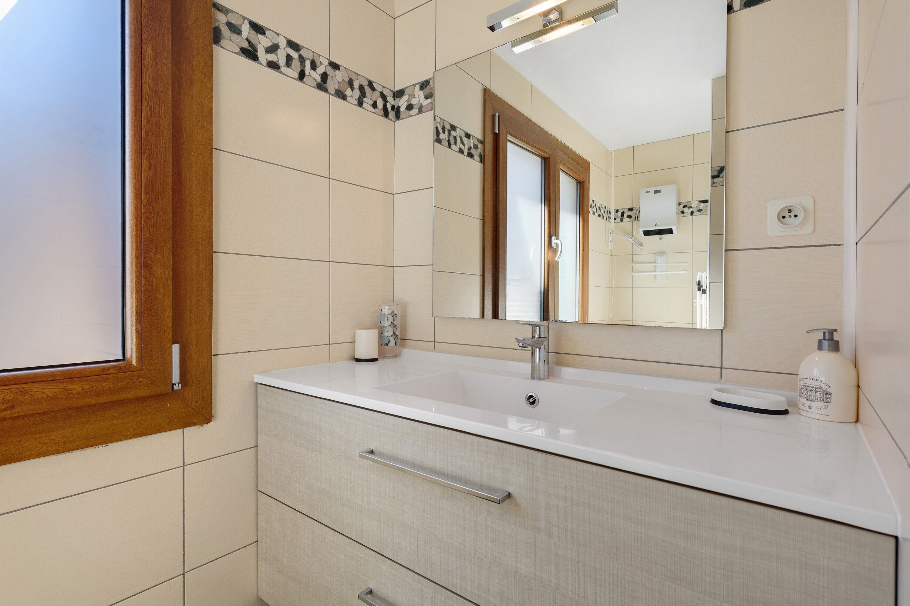 Une salle de bain avec un lavabo blanc, un miroir, une fenêtre et un porte-serviettes.