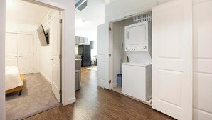 A hallway with a bed, a washing machine, and a kitchen area. - Landing | Incredible 2BD, Pool, Courtyard (Richmond)