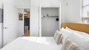 A bedroom with a bed, pillows, a wardrobe, and a bathroom visible through an open door. - Landing | Chic 2BD, Rooftop Lounge, Courtyard (Richmond)