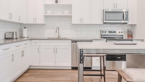 Eine moderne Küche mit weißen Schränken, einer Edelstahl-Mikrowelle, einem Backofen und einem Geschirrspüler.