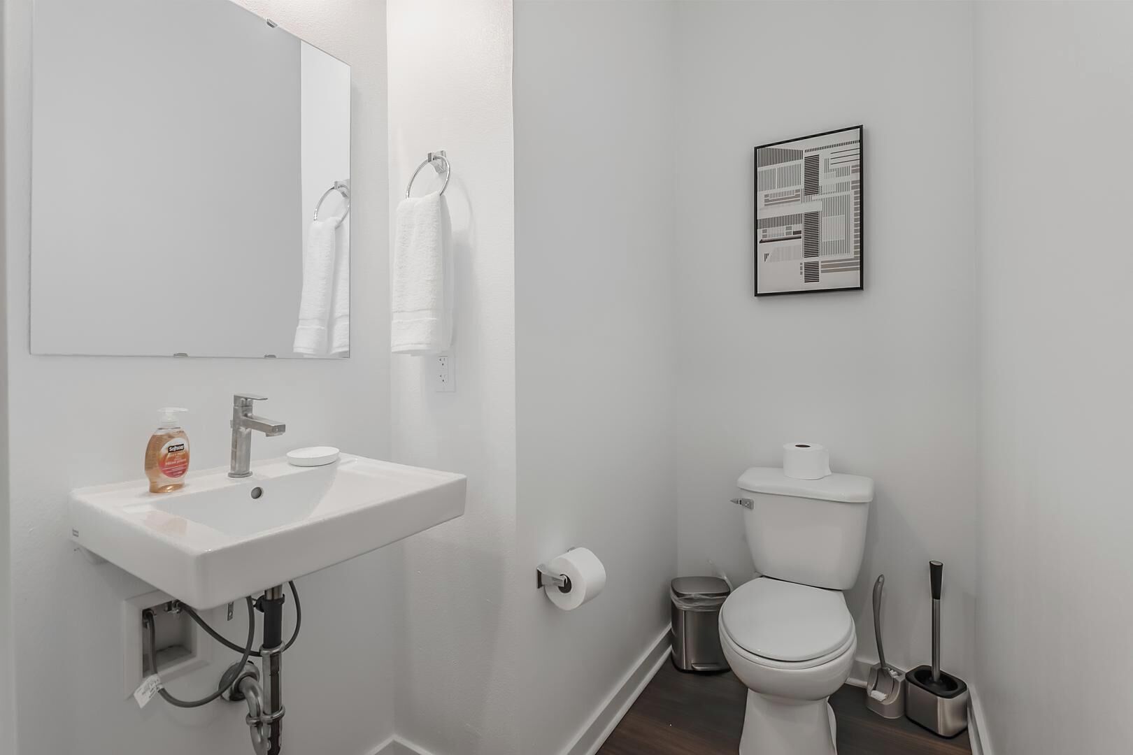 Un baño con lavamanos blanco, espejo, inodoro y un cubo de basura.