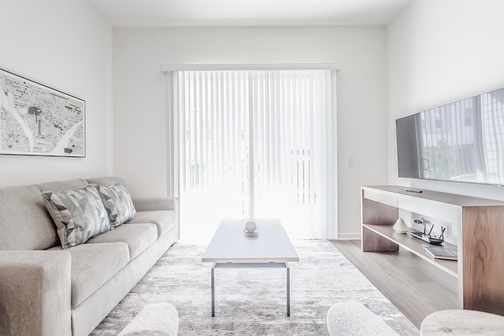 A modern living room with a sofa, a coffee table, a TV, and a large window with blinds.