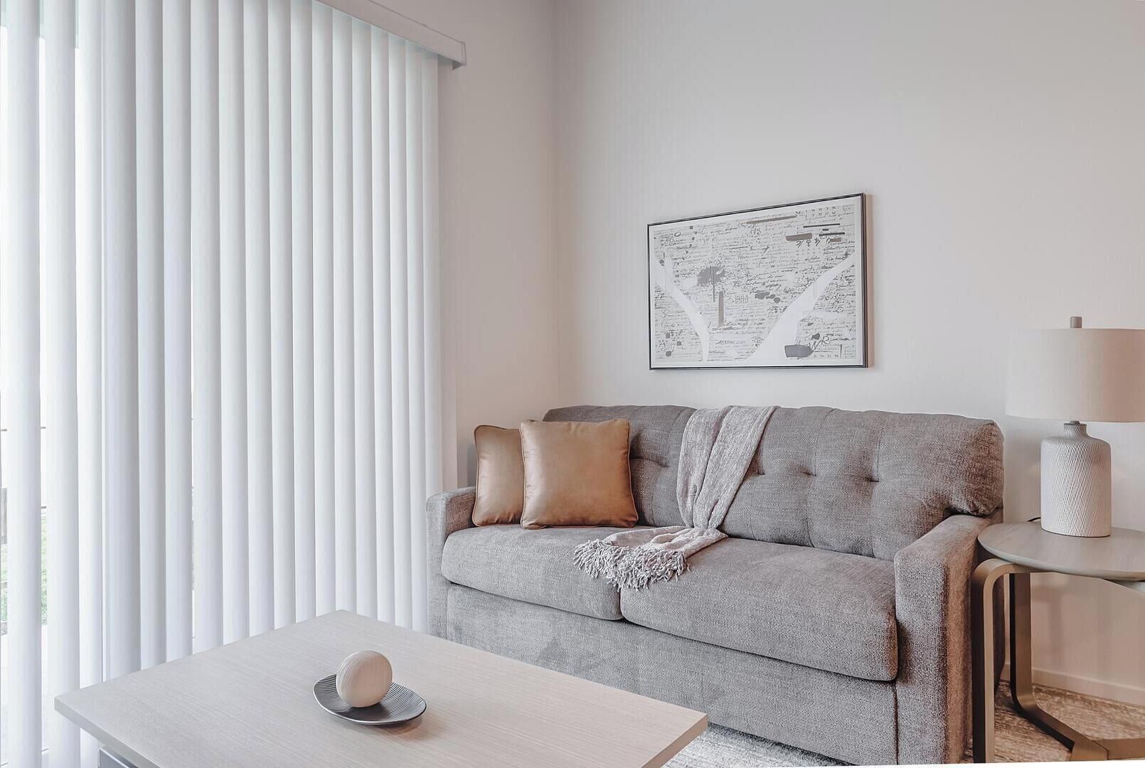 A modern living room with a grey sofa, a small table with a decorative item, a lamp, and a framed map on the wall.