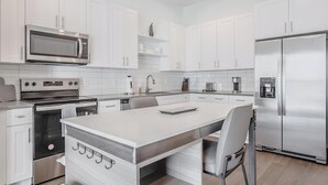 Una cocina moderna con armarios blancos, electrodomésticos de acero inoxidable y una isla central con asientos.