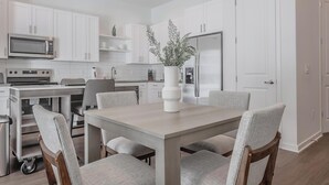 Una cocina moderna con armarios blancos, un refrigerador de acero inoxidable, un microondas y una estufa. Hay una mesa de comedor con cuatro sillas y un florero con flores.