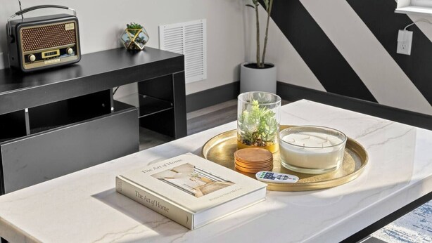 A modern living room with a marble coffee table, a book titled 'The Art of Home', a candle, and a decorative tray. - Sunny 1BR Apt Near Music Scene! (Nashville)
