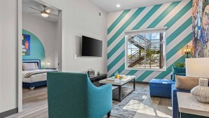 A modern living room with a large TV, a sofa, a coffee table, and a staircase visible through a window. - Sunny 1BR Apt Near Music Scene! (Nashville)