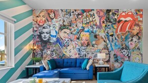 A living room with a blue sofa, a coffee table, and a wall covered with pop art. - Sunny 1BR Apt Near Music Scene! (Nashville)
