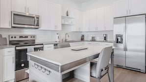 A modern kitchen with white cabinetry, stainless steel appliances, and a central island with seating. - Landing | Stylish 3BD, Gym (Four Corners)