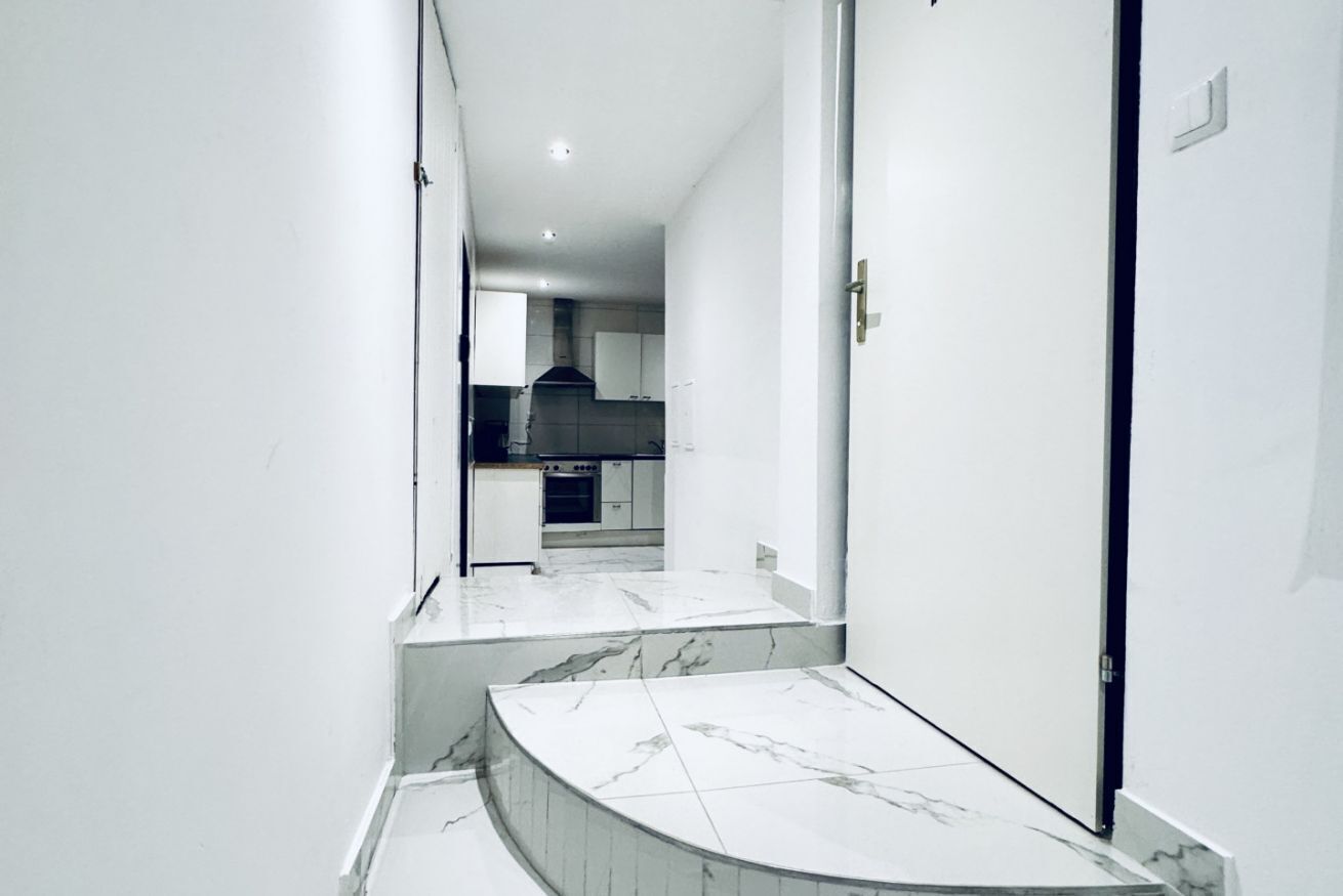 Un couloir étroit avec un escalier en marbre menant à une cuisine.