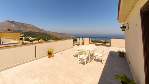 Eine Terrasse mit Tisch und Stühlen, Blumentöpfen und Blick auf das Meer und die Berge.