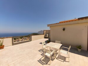 Eine Terrasse mit Tisch und Stühlen, einem Blumentopf und Blick auf das Meer.