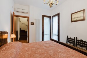A bedroom with a bed, a chandelier, a framed picture, and a window with curtains. - Ciciliana: Tranquility and Panoramic Views in Sicily (Valderice)