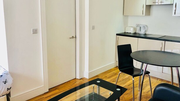 A modern kitchen with a black countertop, white cabinets, and a black chair. - City Sparrow Apartments (London)