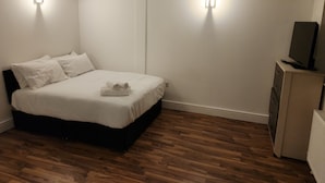 A bedroom with a bed, pillows, a TV on a cabinet, and two wall-mounted lights. - City Sparrow Apartments (London)