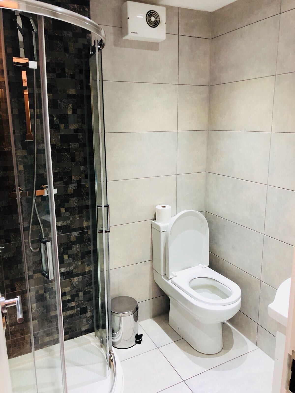 A modern bathroom with a glass-enclosed shower, a toilet, and a trash can.
