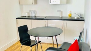 A modern kitchen with a round dining table, black chairs, and a black sofa with red cushions. - City Sparrow Apartments (London)
