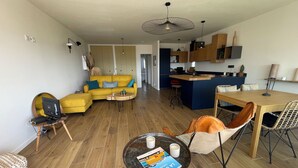 Ein modernes Wohnzimmer mit einem gelben Sofa, einem Esstisch und einer Küche im Hintergrund.
