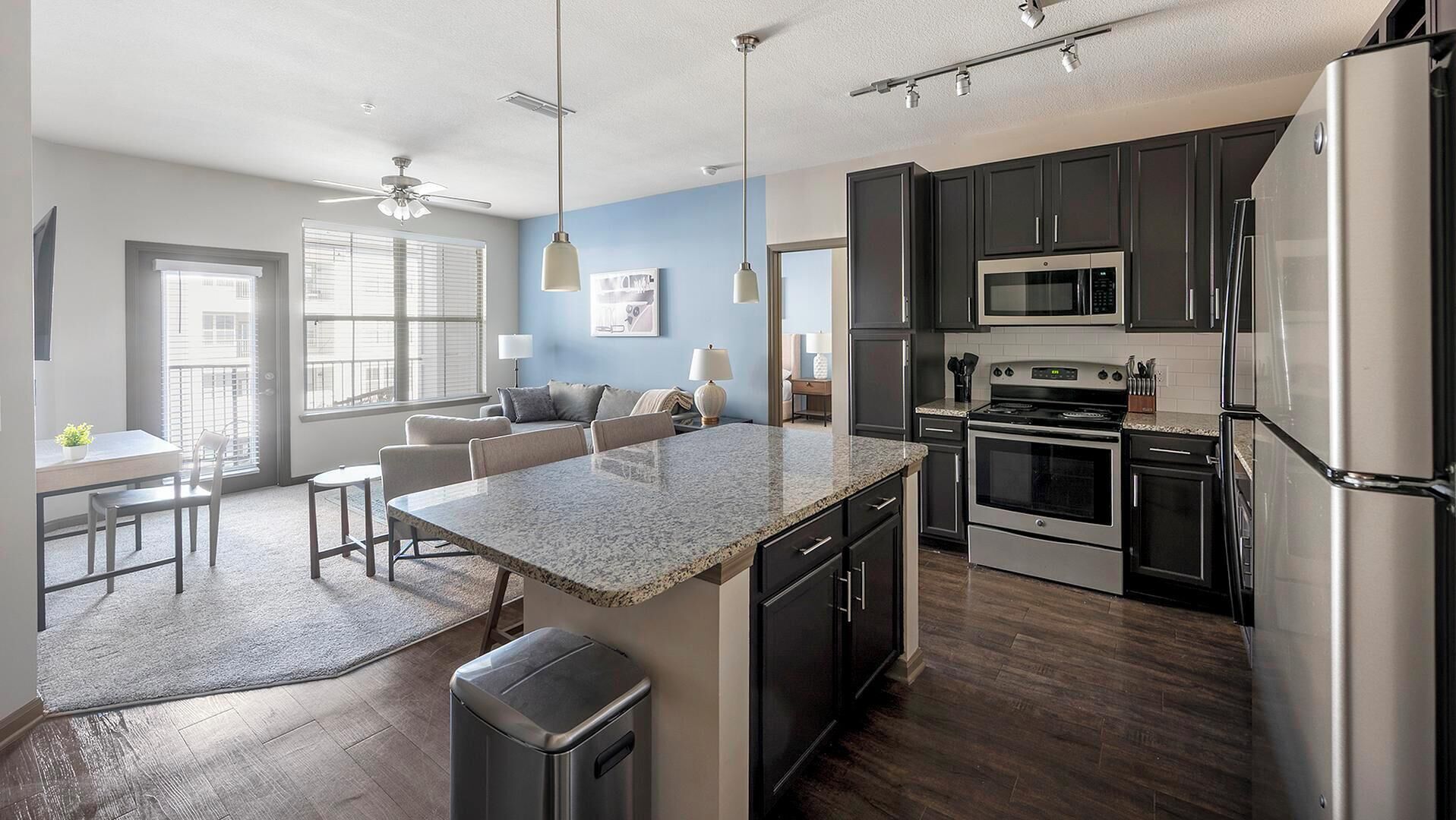 A modern kitchen with dark cabinets, stainless steel appliances, and a granite countertop island.