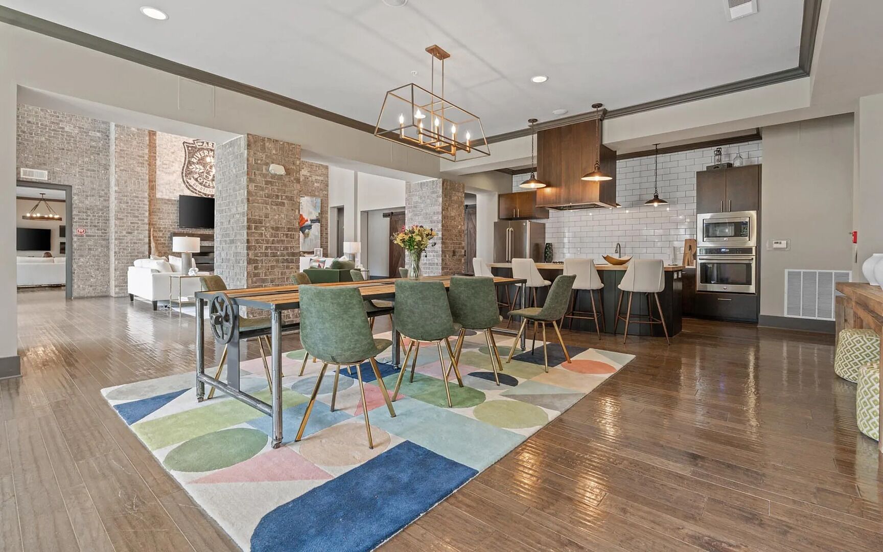 Una cocina moderna con una isla central, taburetes de bar y un comedor con un tapete colorido.