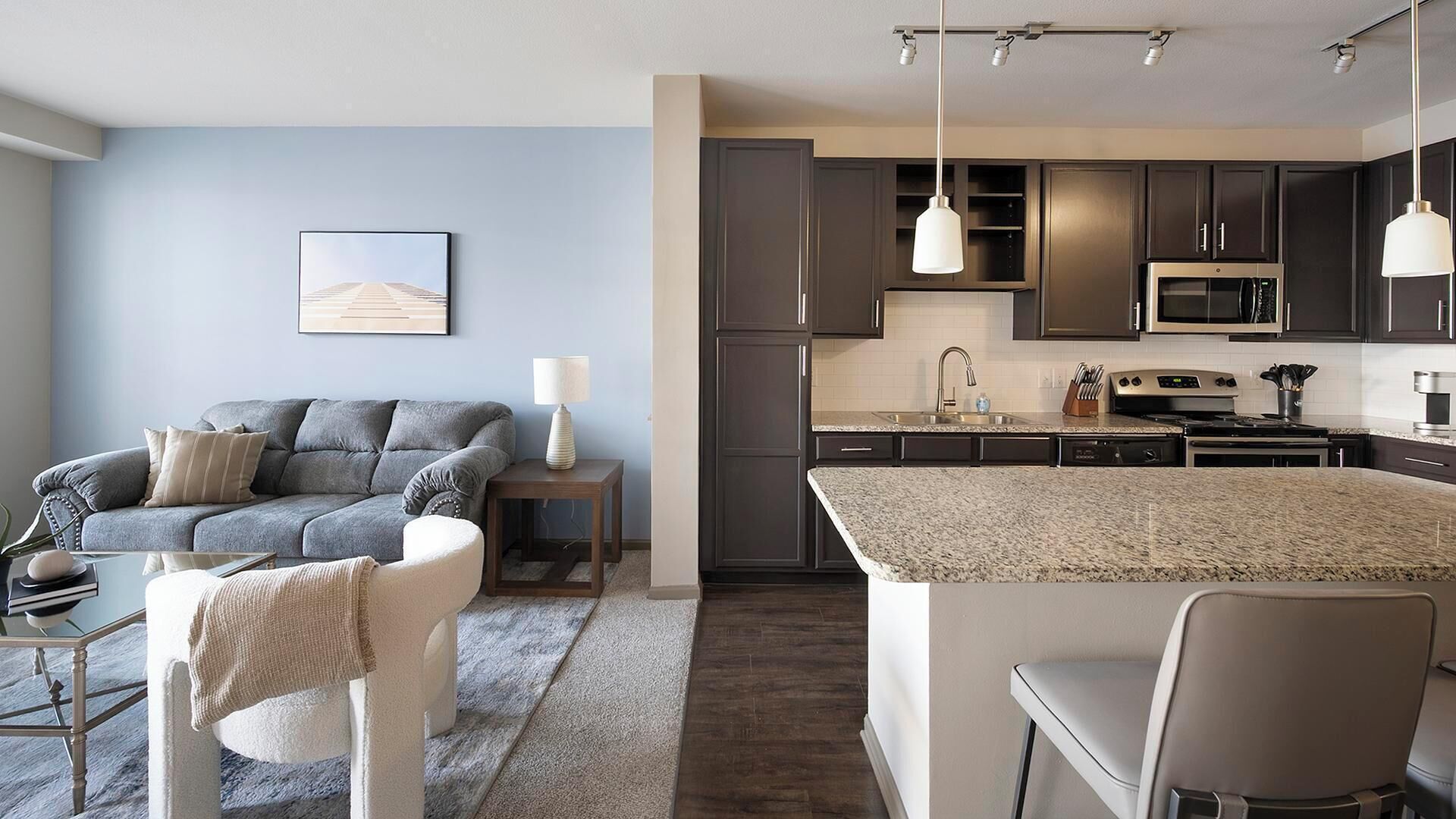 A modern kitchen with dark cabinets, a granite countertop, and stainless steel appliances.