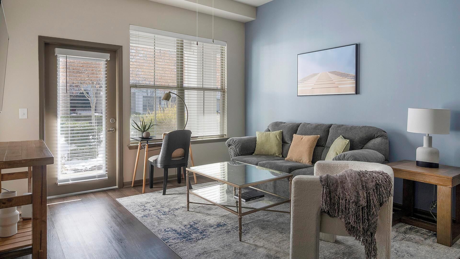 A modern living room with a grey sofa, a glass coffee table, and a lamp on a side table.
