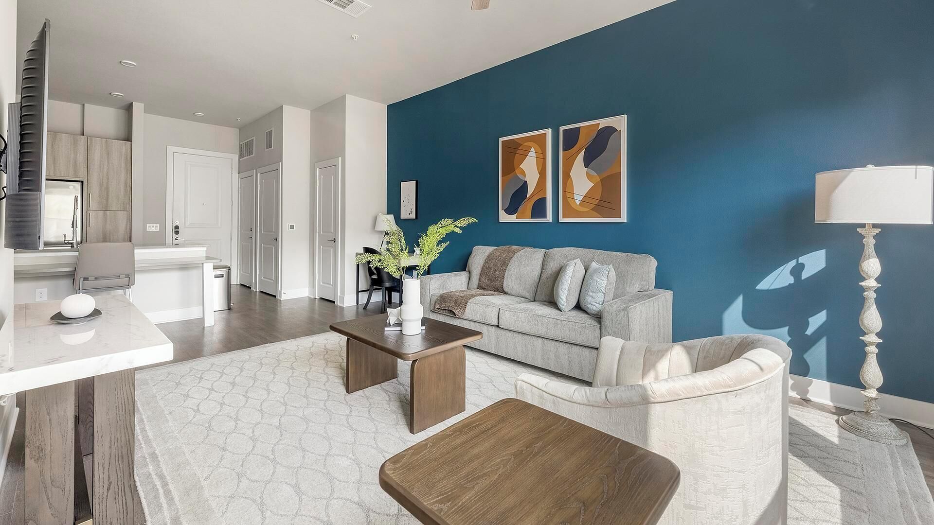 Un salon moderne avec un mur d’accent bleu, un canapé, une table basse et un coin repas comprenant une table et des chaises blanches.