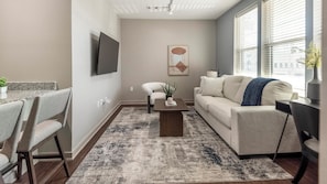 Un salon moderne comprenant un canapé, des fauteuils, une table basse et un téléviseur à écran plat fixé au mur.
