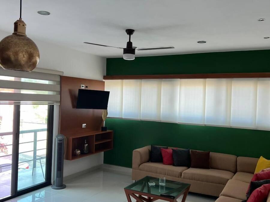 A modern living room with a green accent wall, a beige sofa, a glass coffee table, and a ceiling fan.