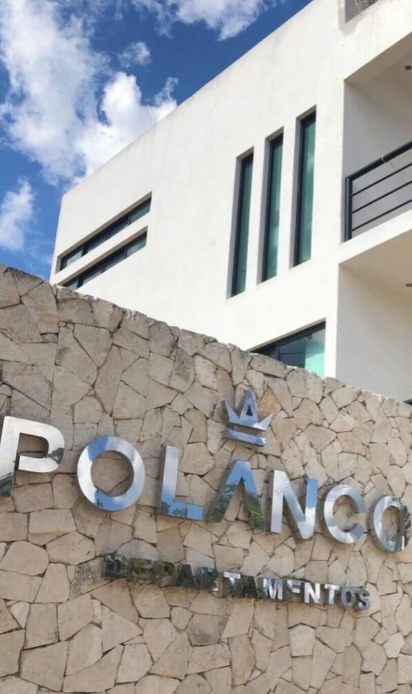 A building with a sign that reads "POLANCO DEPARTAMENTOS" on a stone wall. - Departamentos Polanco (Valladolid)