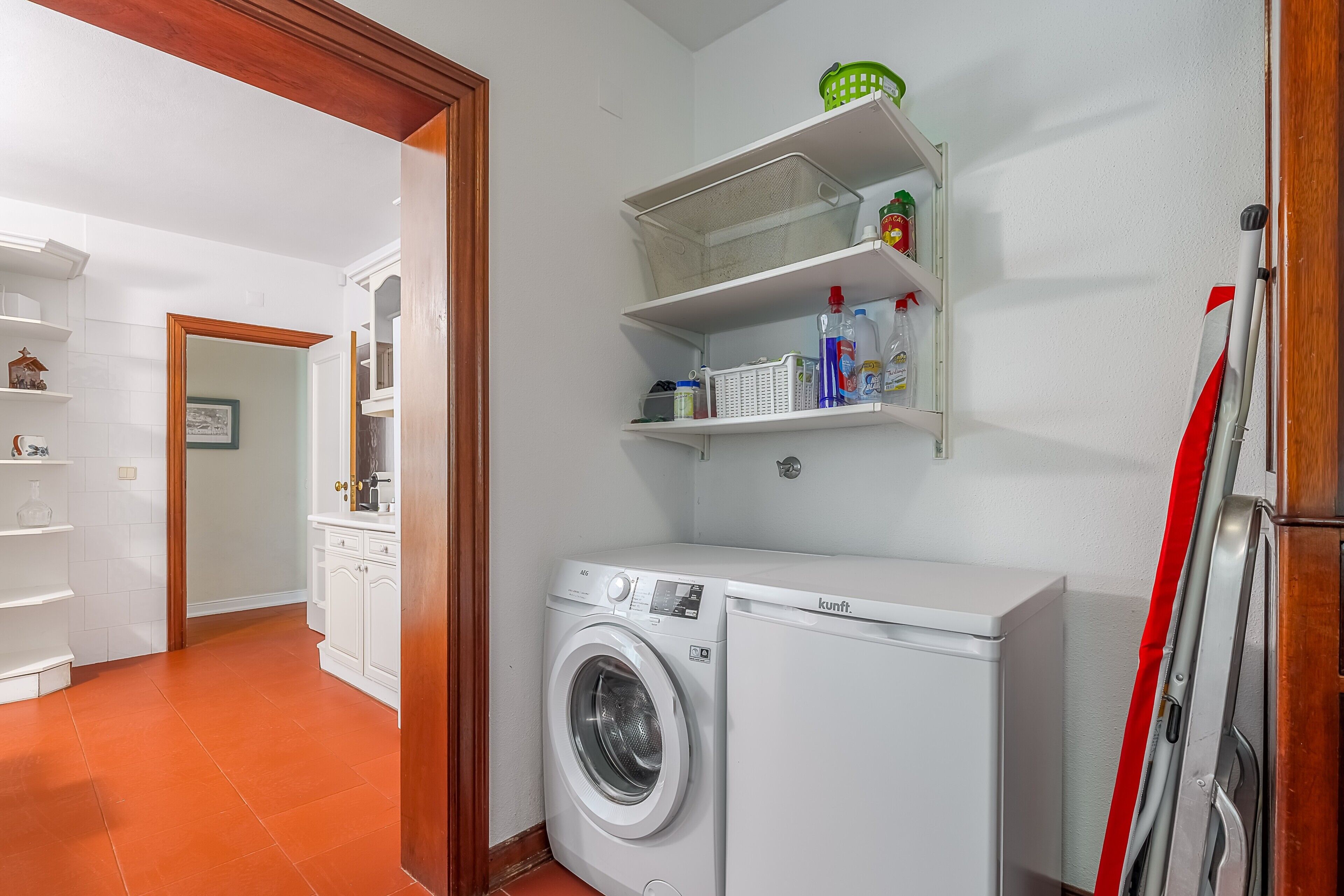 A laundry area with a washing machine, shelves with toiletries, and a door leading to another room.