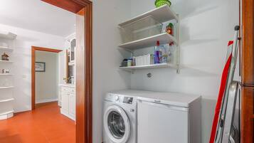A laundry area with a washing machine, shelves with toiletries, and a door leading to another room.