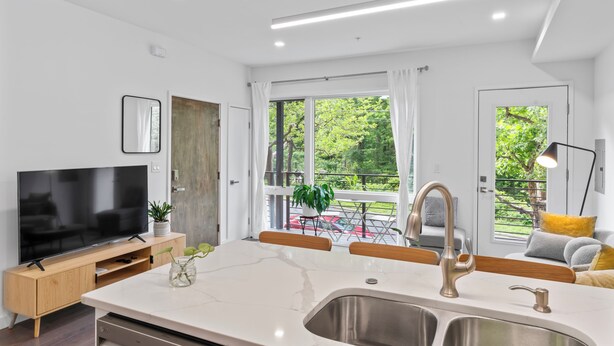 Una cocina moderna con un televisor grande, armarios de madera, encimera de mármol y un lavamanos.