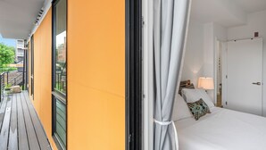 Una habitación de hotel con balcón, una cama con almohadas, una mesita de noche y una puerta.