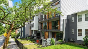 Un moderno edificio de apartamentos de varios pisos con balcones, un patio cercado y un árbol.