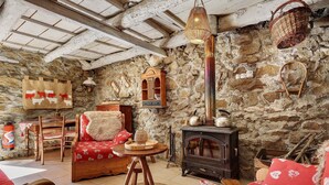 Un interior rústico con pared de piedra, mobiliario de madera, chimenea y una cesta colgante.