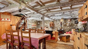Un interior rústico con una mesa de comedor de madera, sillas, una pared de piedra y una escalera.