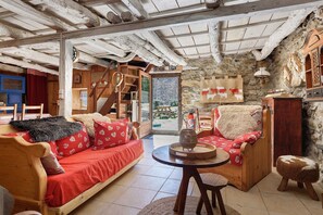 A rustic interior with a wooden sofa, a round wooden table, and a stone wall. - Secret Shepherd’s Hut: A Peaceful Retreat in Nature (GAVARNIE-GÈDRE)