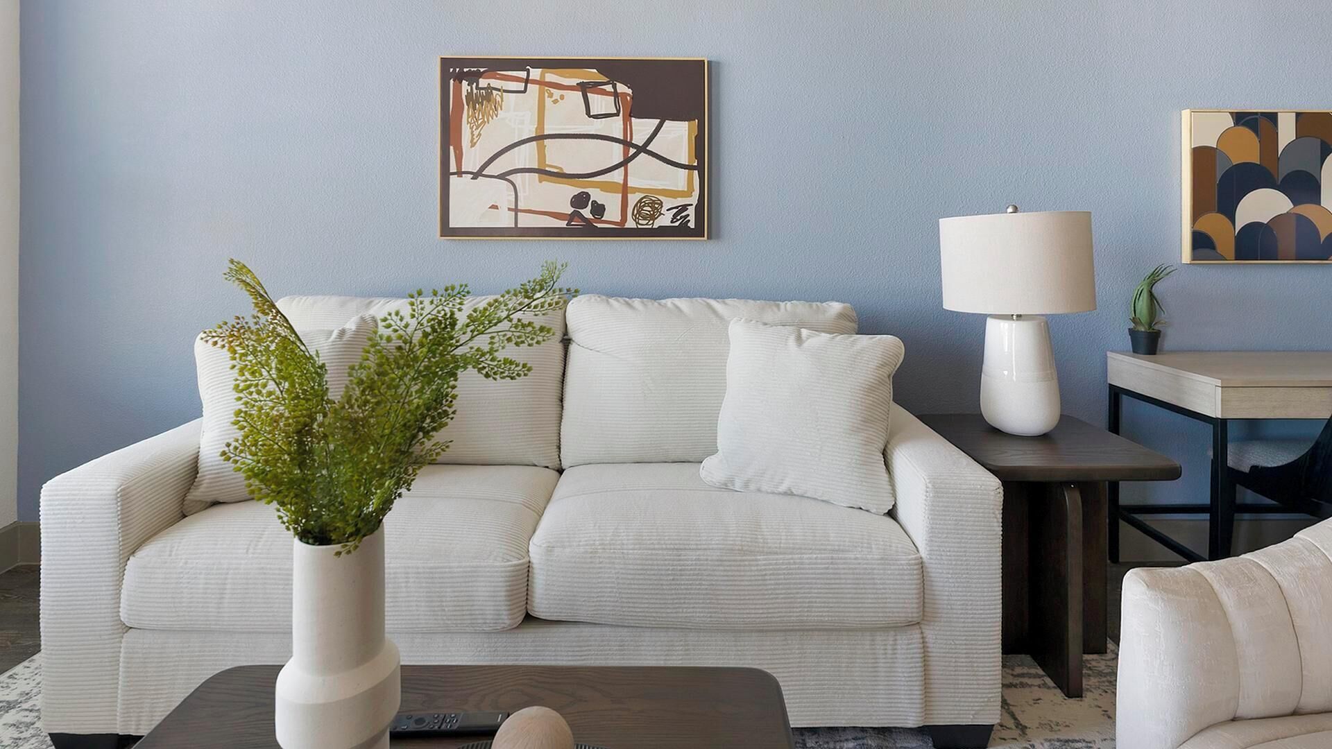 Ein Wohnzimmer mit einem hellen Sofa, einem Couchtisch, einer Lampe und einem Gemälde an der Wand.