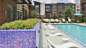 Une piscine avec un bord carrelé, des chaises longues et un parterre de fleurs.