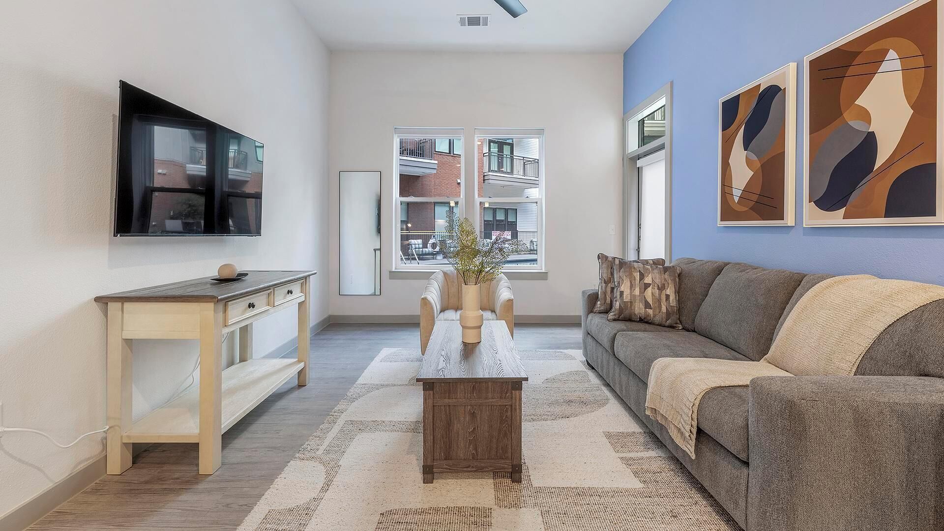 A modern living room with a flat-screen TV, a wooden side table, a sofa, and abstract wall art.