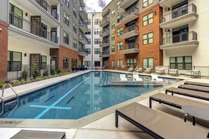 A modern apartment building with a central swimming pool, outdoor seating, and multiple balconies. - Landing | Spectacular 1BD, Gym, Pool (Austin)