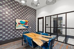 Une salle de conférence avec un mur orné de motifs, une table en bois, des chaises bleues et une cloison en verre.