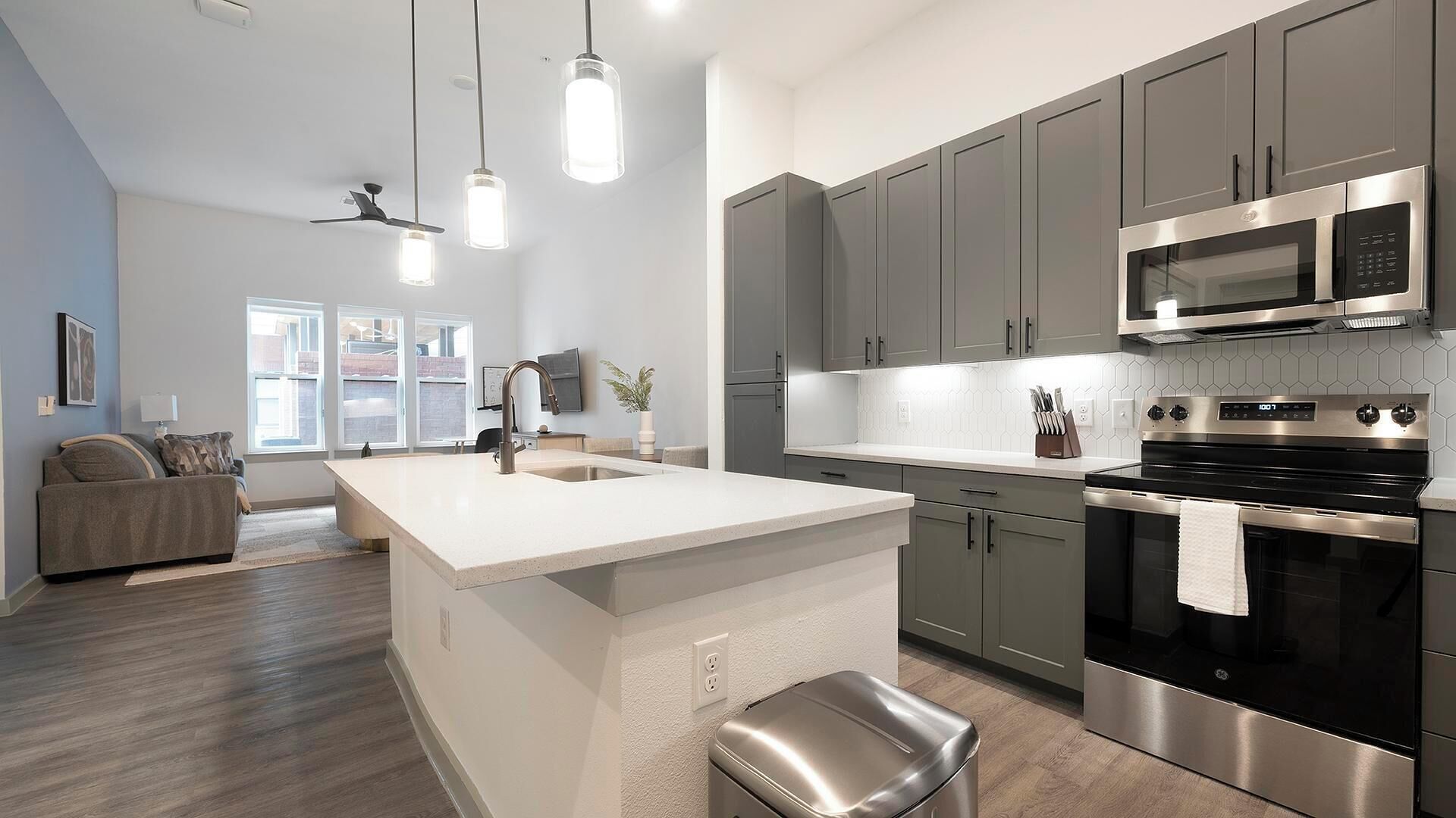 A modern kitchen with grey cabinets, a stainless steel microwave, and a large island with a sink.