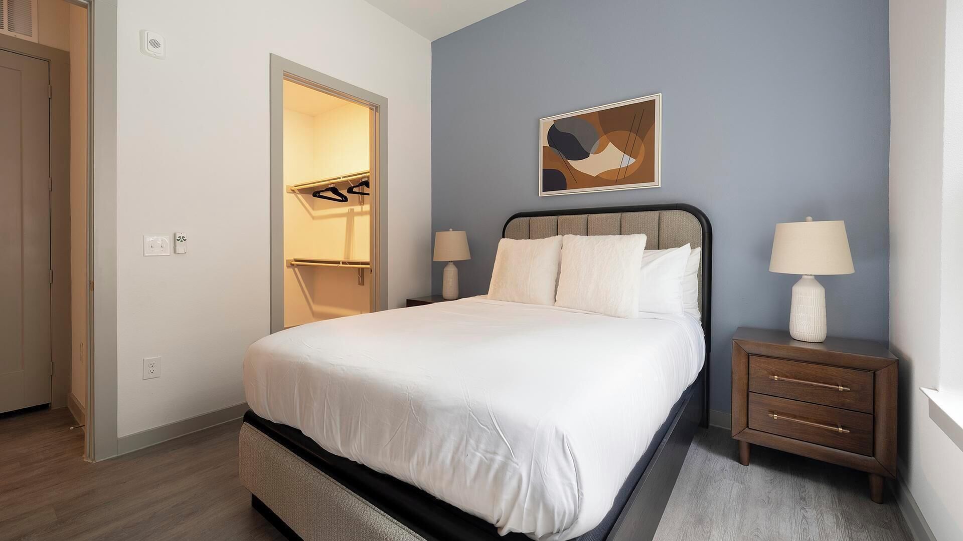 A bedroom with a bed, bedside tables, a nightstand, a painting on the wall, and a closet with a mirror.