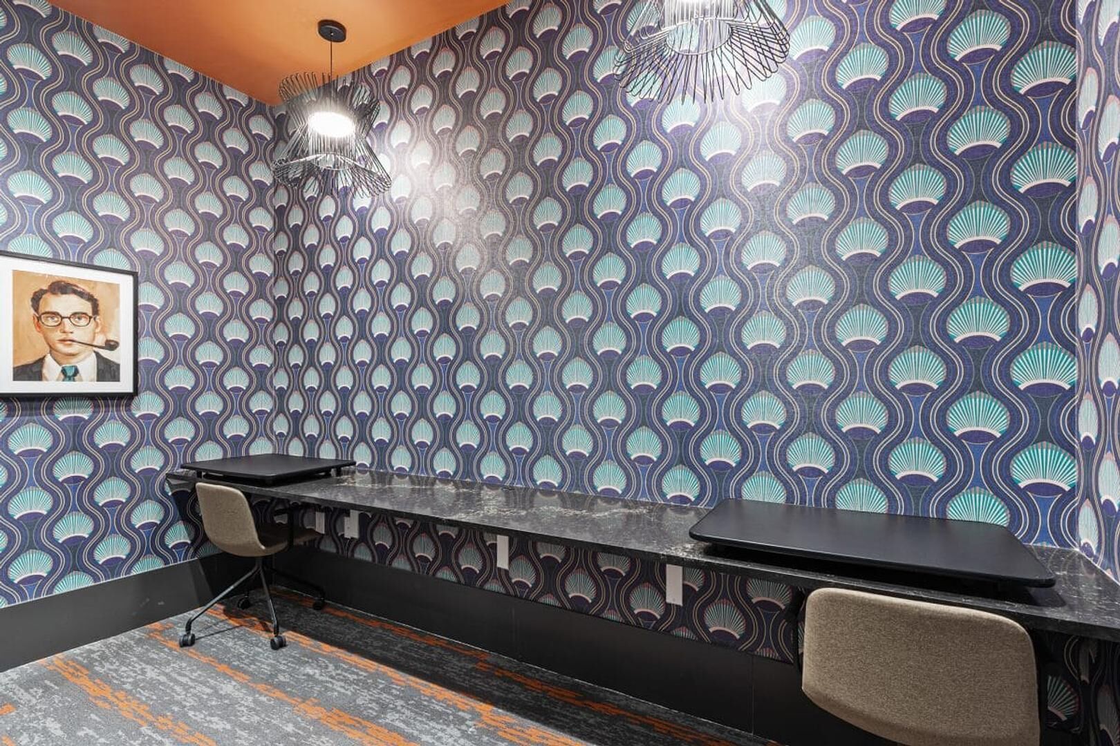 A conference room with a patterned wallpaper, a long table, two chairs, and a hanging light fixture.