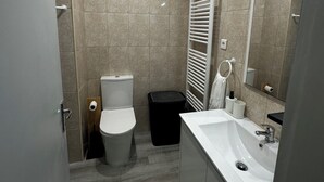 Een moderne badkamer met toilet, bidet, wastafel en spiegel.